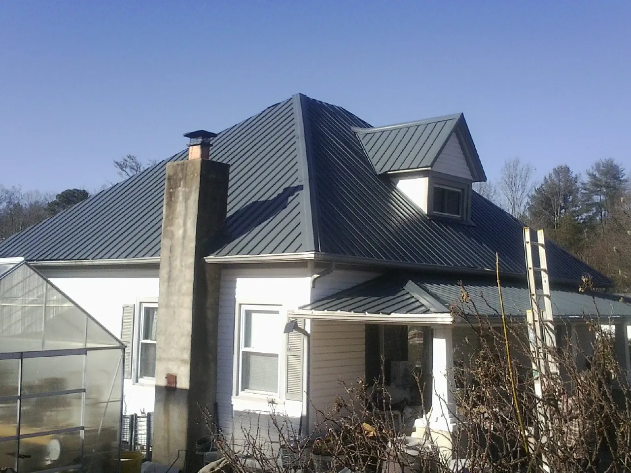 Dark blue standing seam metal roof on a white farmhouse with dormer in Troy