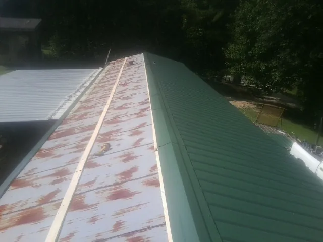 Old rusted panels beside newly installed green metal roofing — Wind Damage Roof Repair by Roofing Brothers in Troy
